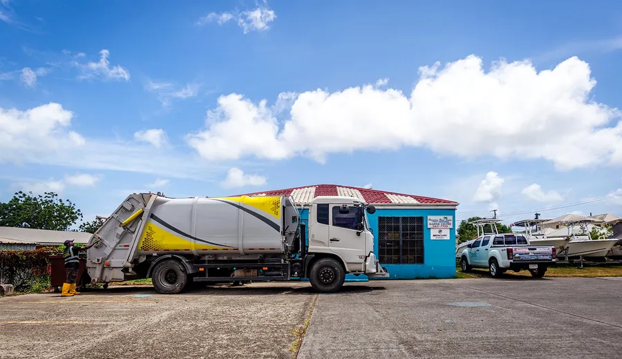 Island Sanitation Plus rear-loader bin truck parked beside a commercial building