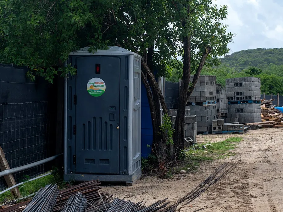 Island Sanitation Plus standard portable toilet unit on a construction site, next to rebar and concrete block