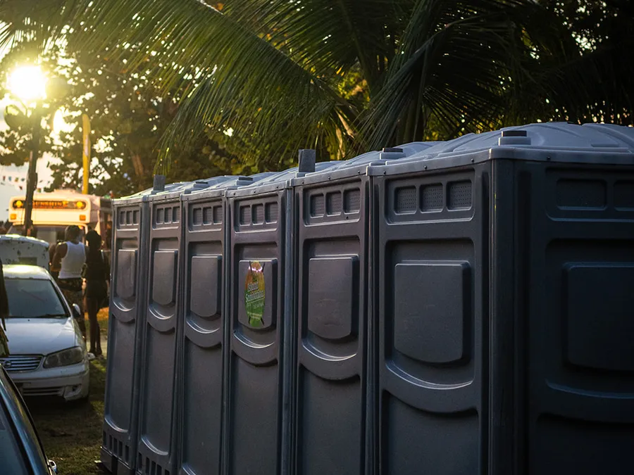 Row of Island Sanitation Plus portable toilet units set up at an outdoor event at sunset, palm trees behind