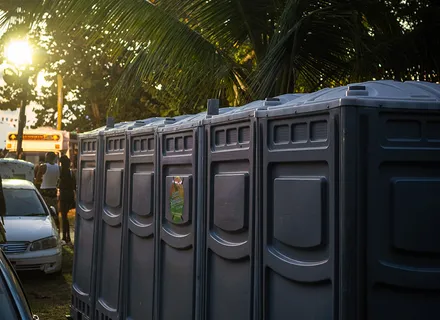 Row of Island Sanitation Plus portable toilet units set up at an outdoor event at sunset, palm trees behind