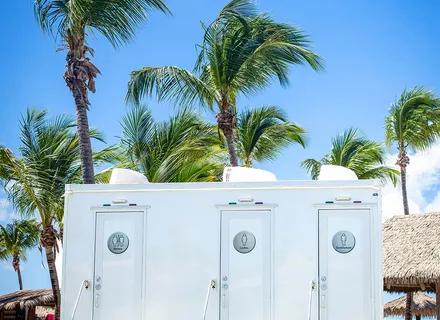 Island Sanitation Plus VIP restroom trailer set up among palm trees at a resort venue