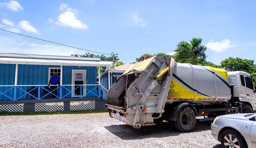 Island Sanitation Plus rear-loader truck with compactor door open, servicing a commercial site