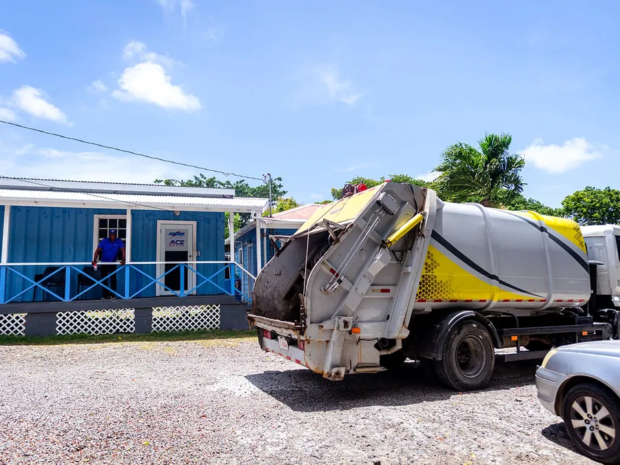 Island Sanitation Plus rear-loader truck with compactor door open, servicing a commercial site