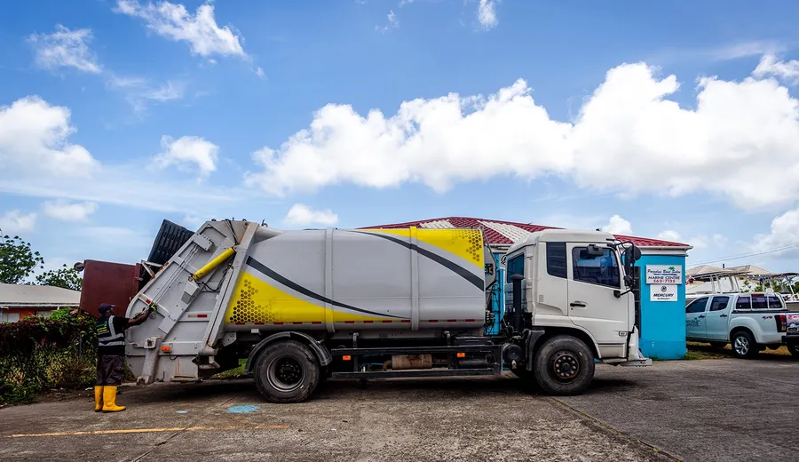 Island Sanitation Plus crew member loading a rear-loader collection truck on a commercial site